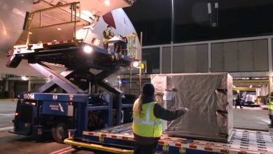 A hydraulic lift raises metal containers with cargo to door of a jet at night.