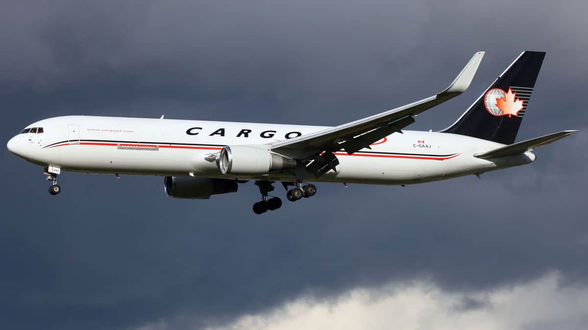 A white jet with a blue tail and the name Cargojet on its side has wheels down as it flies low to start landing.