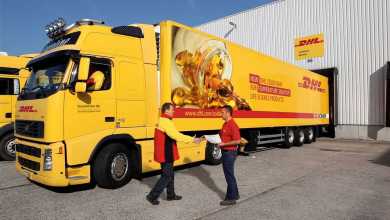 A bright yellow refrigerated DHL truck backed up to loading dock.