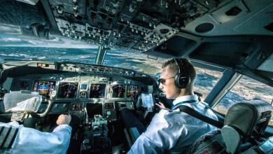 Pilots in cockpit looking out at sky, ground below..