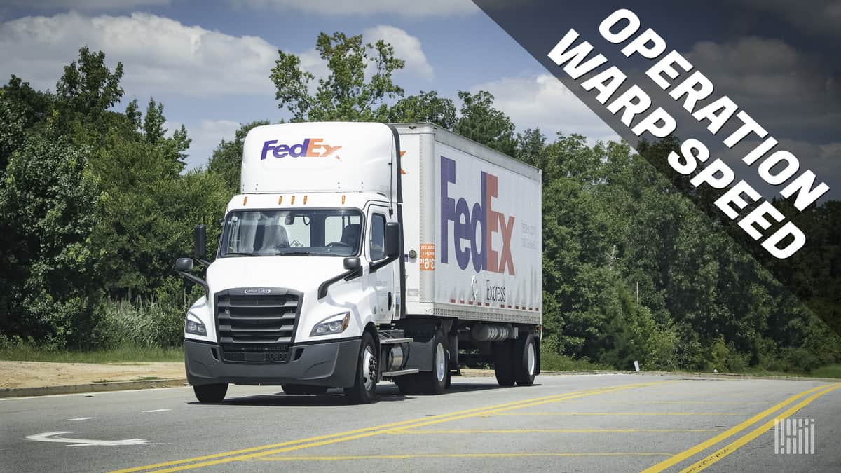 White FedEx truck driving on highway, headed towards us with Operation Warp Speed banner on side of photo for vaccine distribution effort.