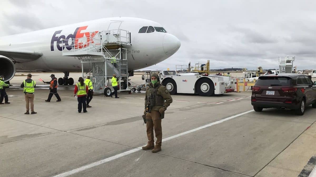 Armed guard on tarmac in front of a FedEx plane getting loaded with COVID vaccine.