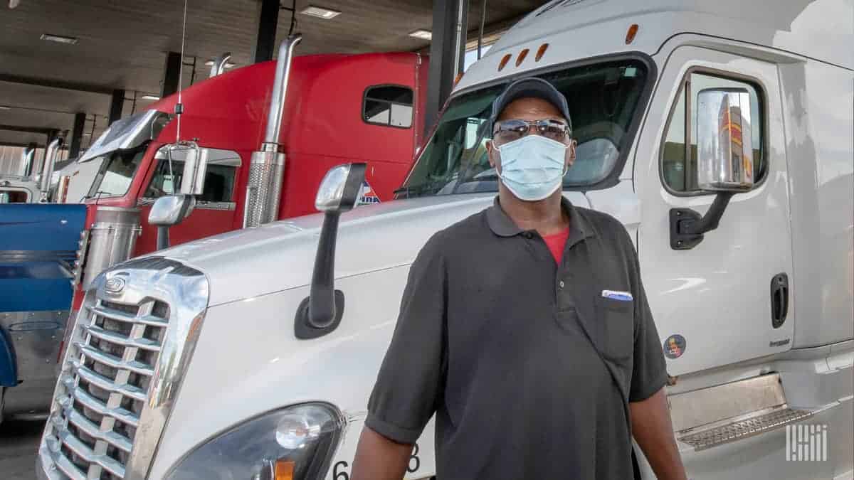 Black man wearing a face mask stands in front of white cab.