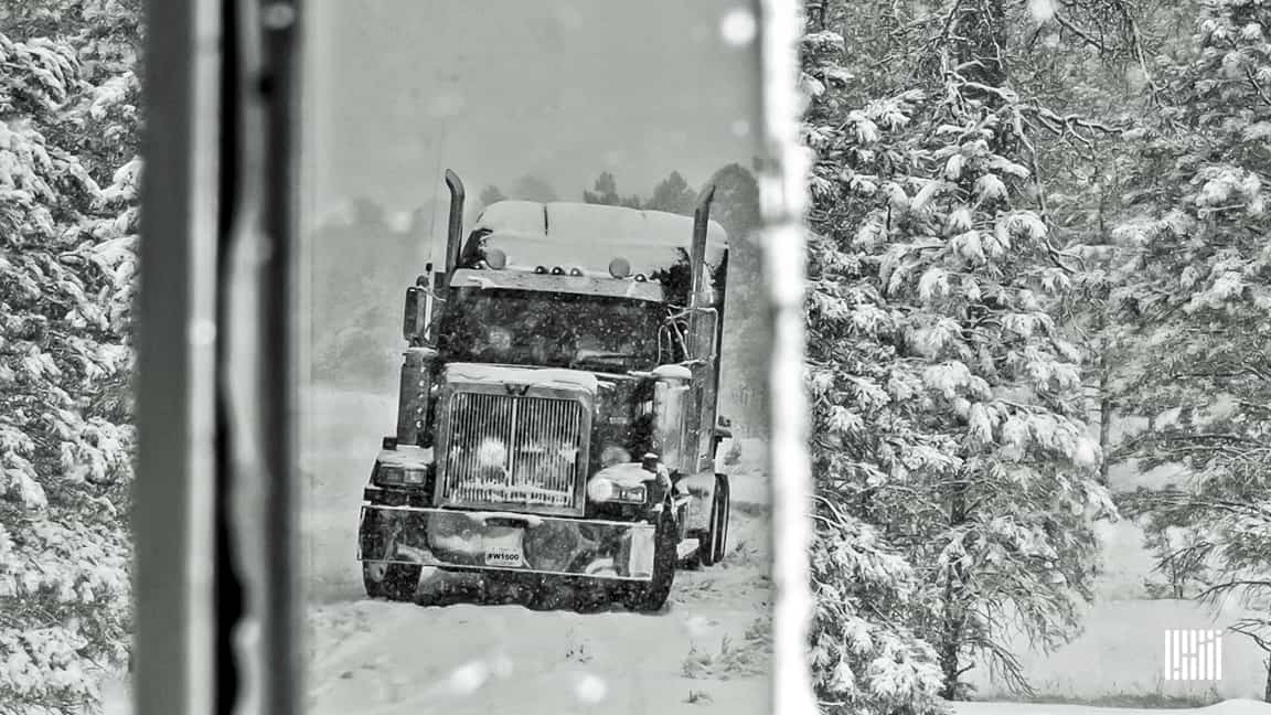 Tractor-trailer heading down snowy highway.