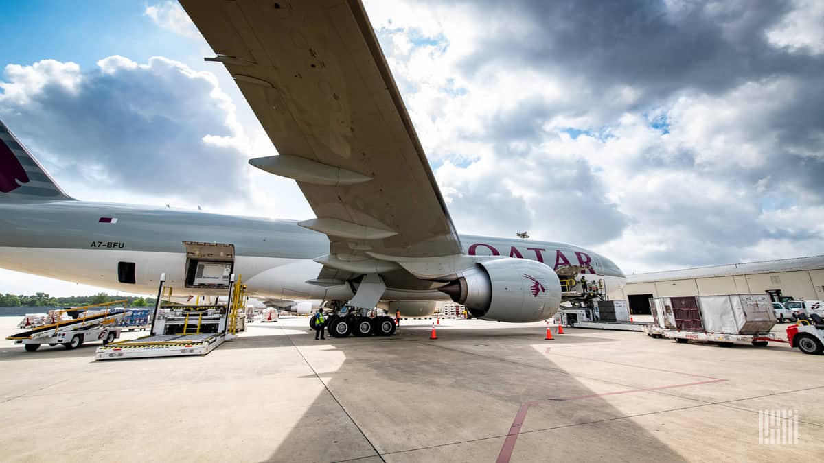 A big cargo plane with door open to load cargo. Photo from side, under wing on a sunny day.