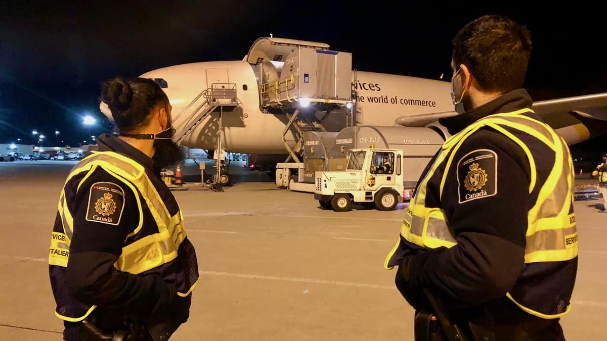 Two Canada Border Services officers watch COVID-19 vaccines get unloaded from a UPS plane that delivered Canada's first shipments.