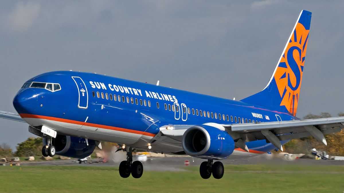 A bright blue Boeing 737 with orange lettering lands on runway.