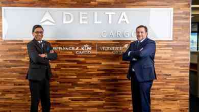 Delta Cargo executives standing in front of company sign at office.