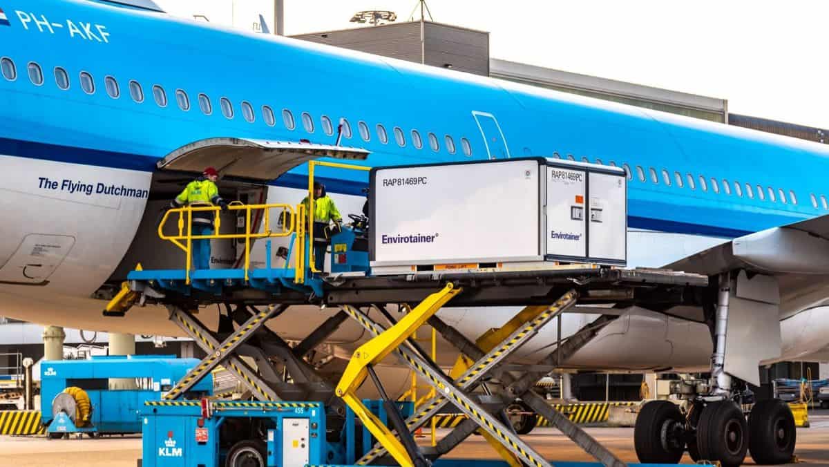 A temperature-controlled container on a lift gets loaded in side of a light blue plane.