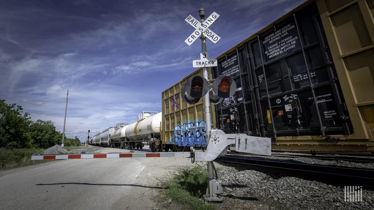 A photograph of a train passing by a railroad crossing.