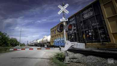 A photograph of a train passing by a railroad crossing.