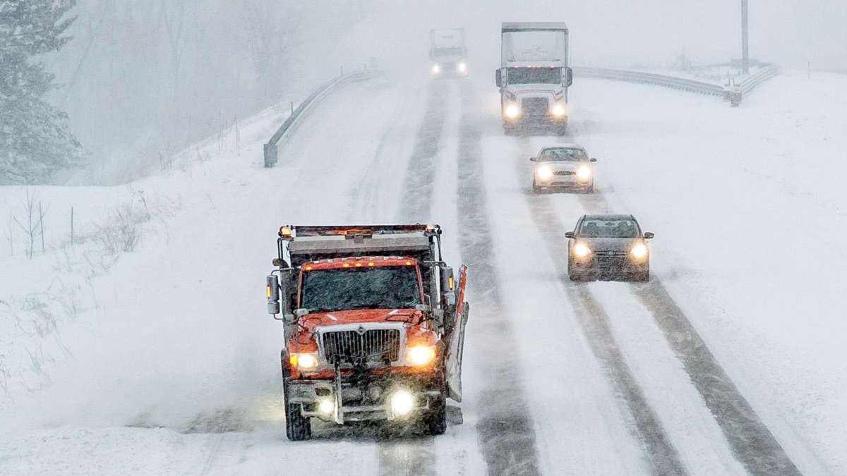 Cars and tractor-trailers behind a snow plow truck clearing a Michigan highway.