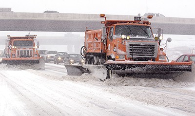 Plow trucks clearing a Minnesota highway, with traffic behind it.