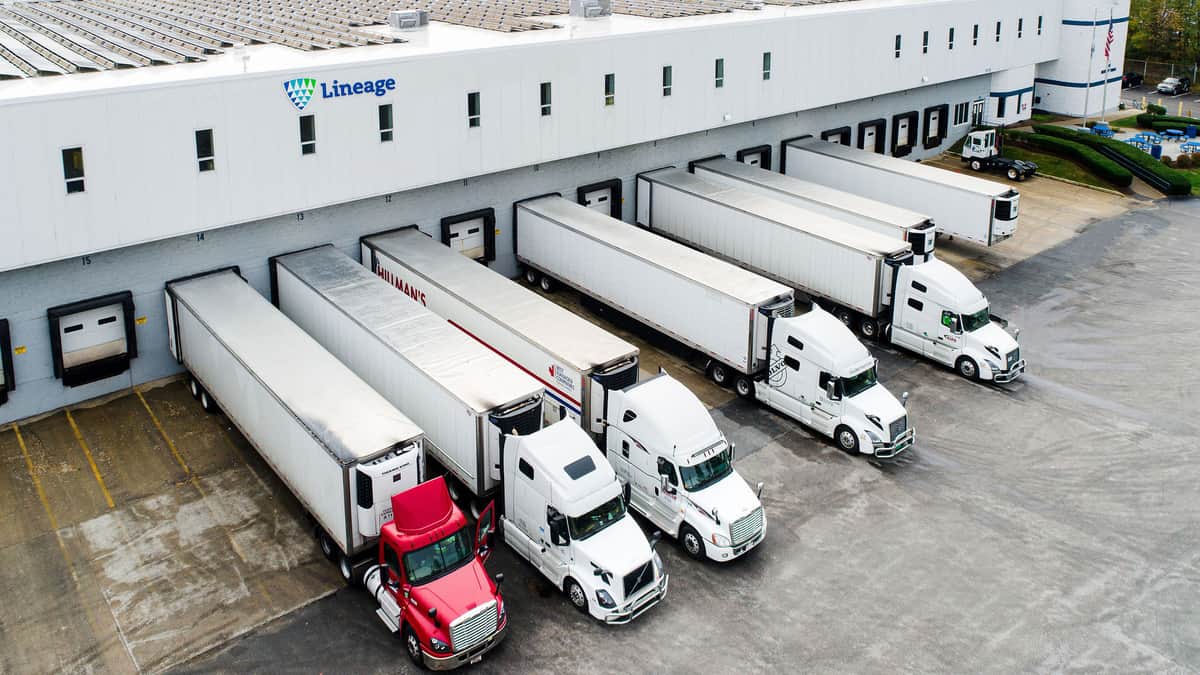A photograph of a warehouse with five trucks parked next to it.