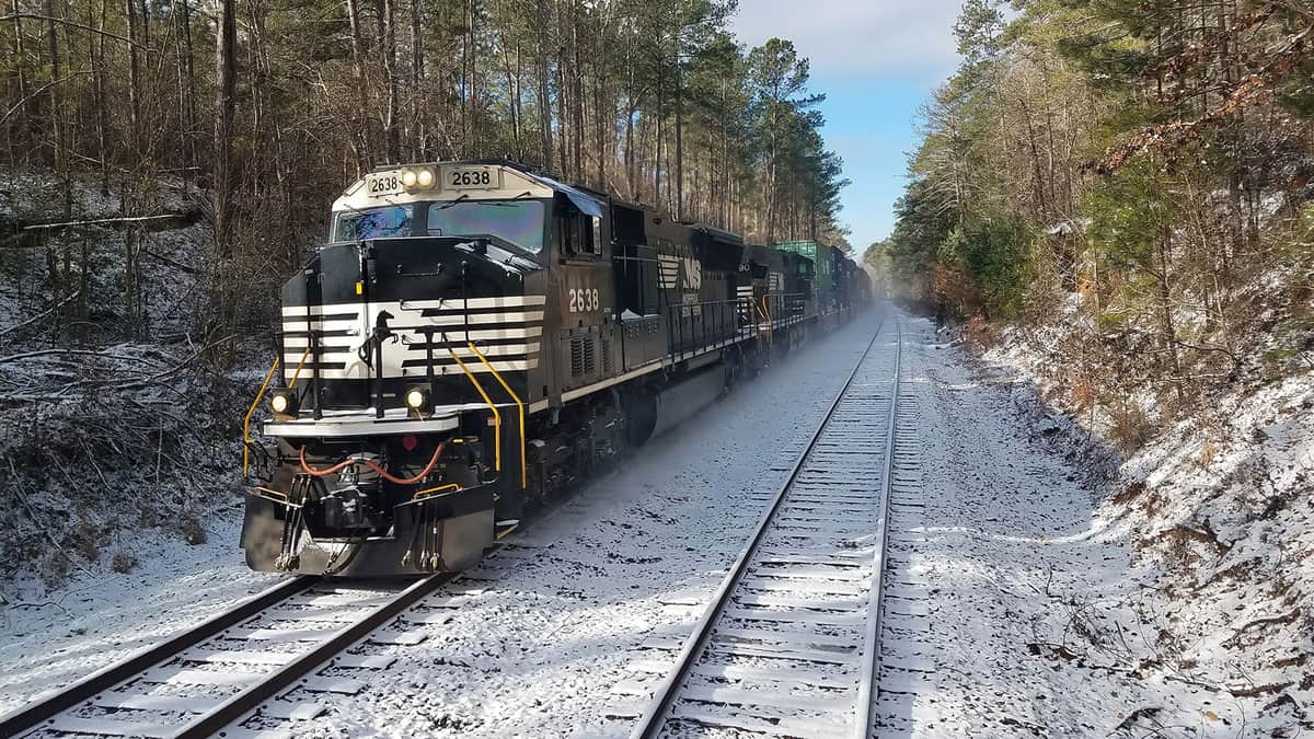 A photograph of a Norfolk Southern train traveling through the snow.