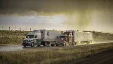 Tractor-trailers heading down highway with storm cloud on the horizon.