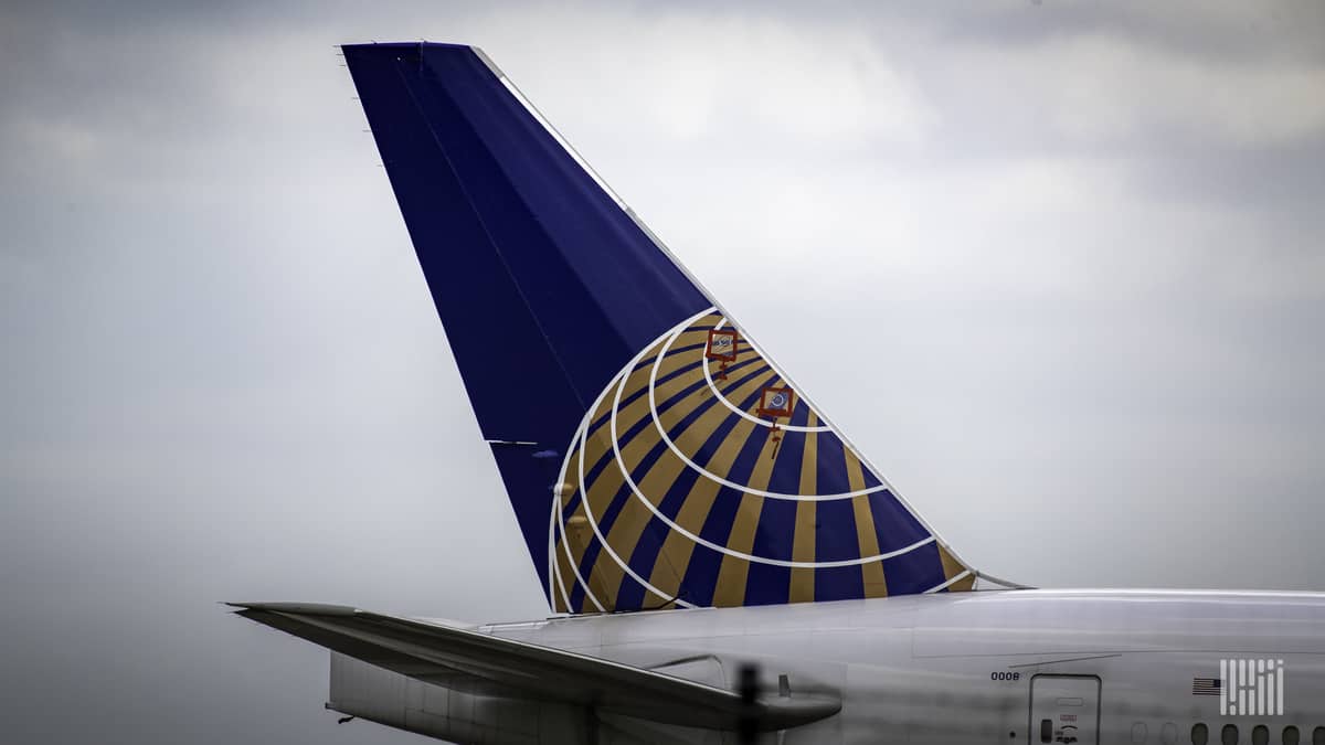 Blue tail fin of a United jet against a gray sky.