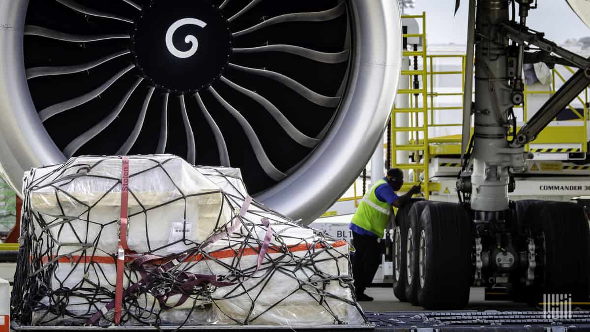 A cargo pallet rests on the ground in front of a big jet engine.