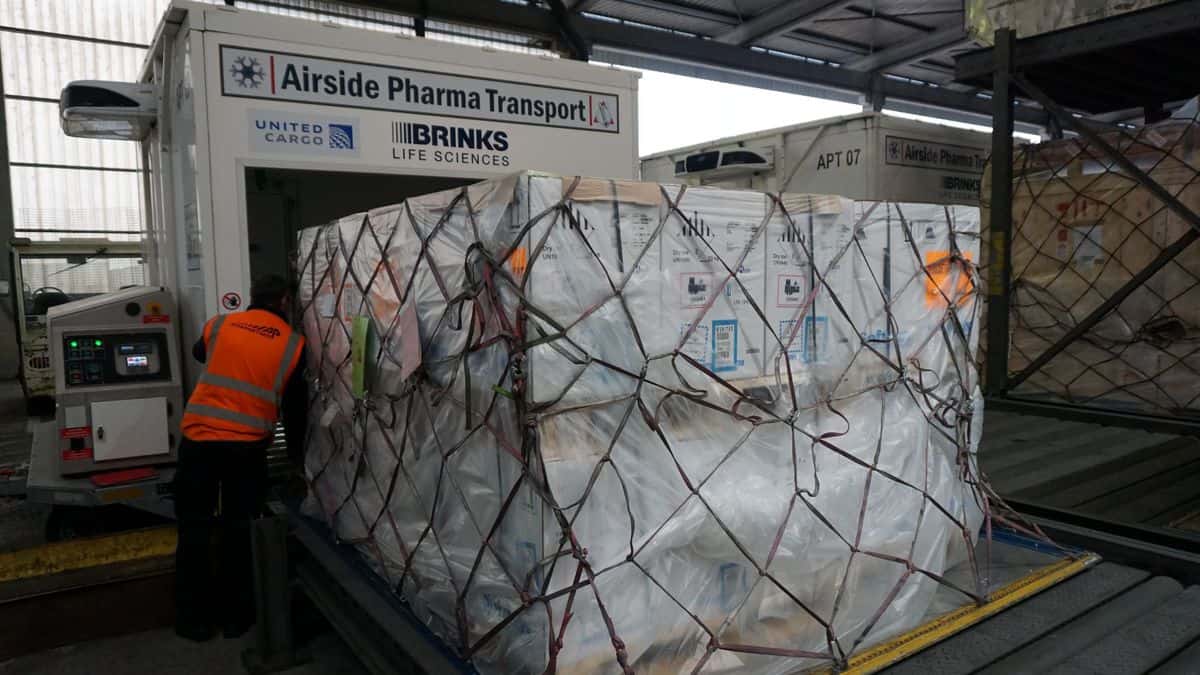 A large pallet of white boxes tied down with netting in an airport terminal.