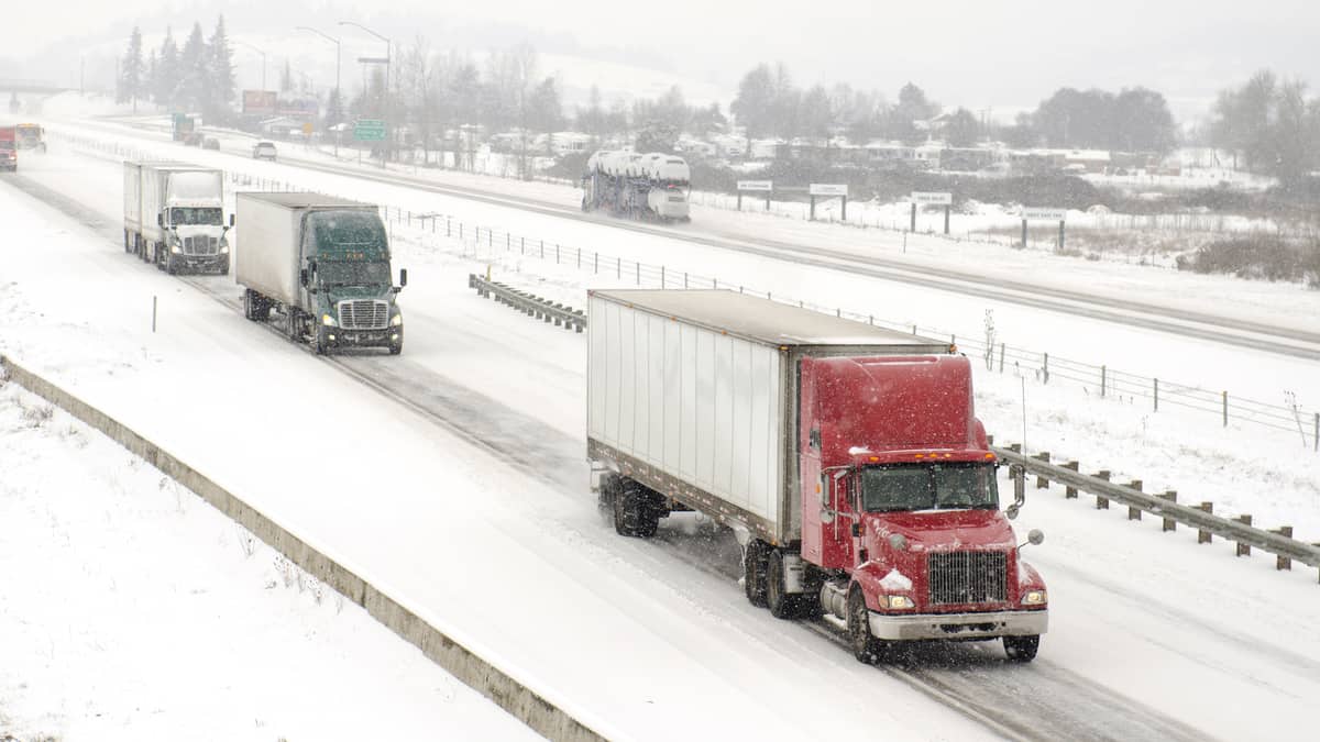 Tractor-trailers heading down snowy highway.