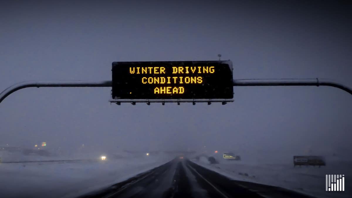 "Winter Driving Conditions Ahead" digital sign above snowy highway.