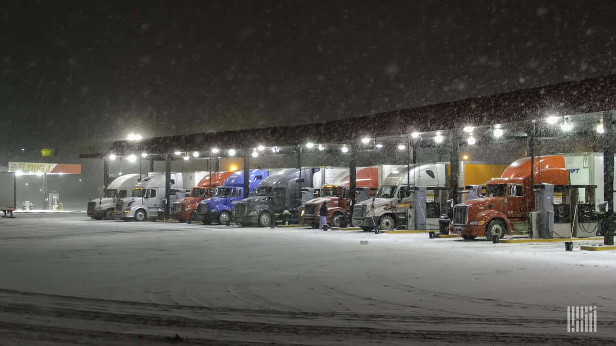 Tractor-trailers parked at a truck stop on a snowy day.