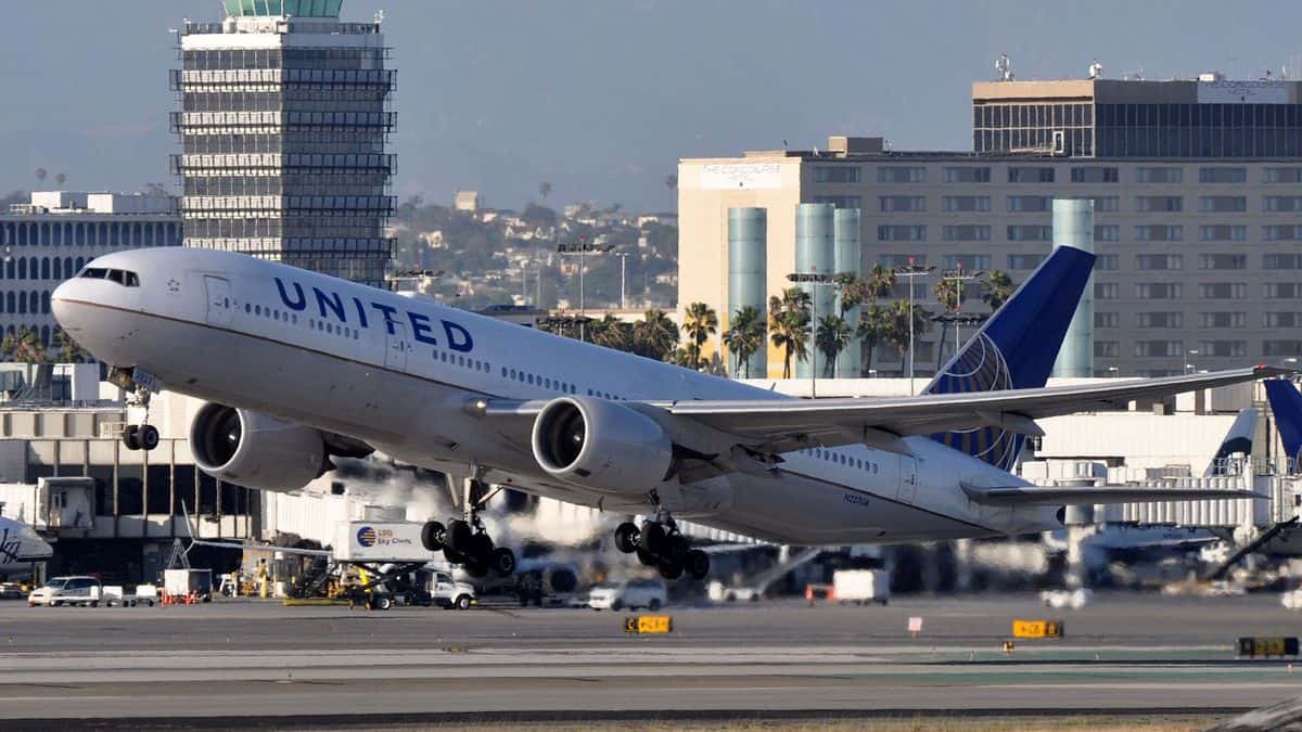 A big United Airlines jet lifts off runway on sunny day at LAX airport.