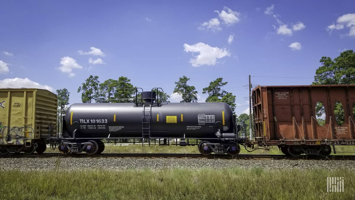 A photograph of a tank car and two railcars parked in a rail yard.