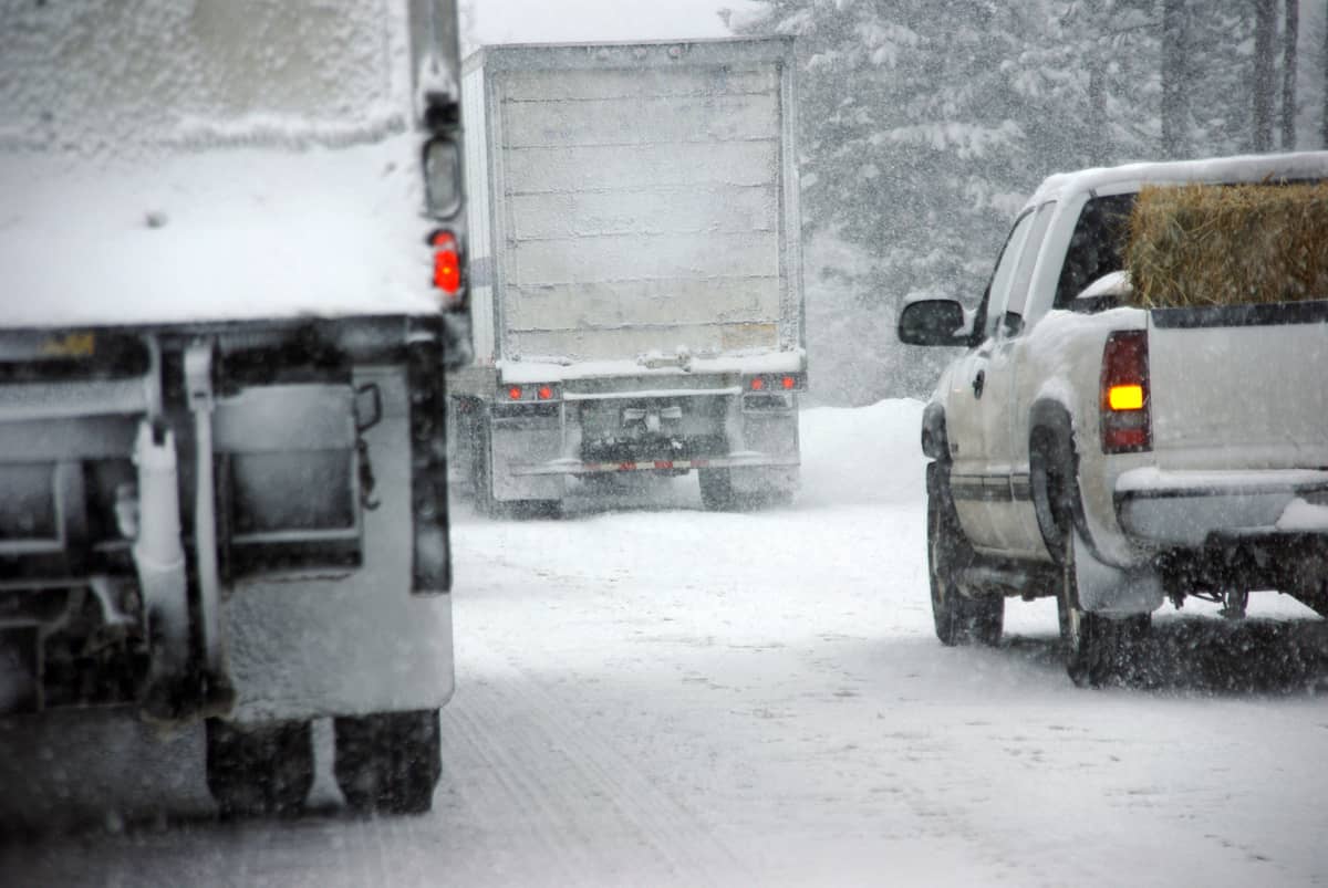 Tractor-trailers heading down a snowy highway.