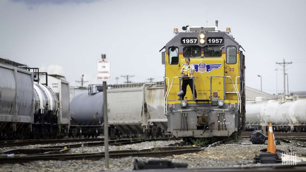 A photograph of a man standing in front of a parked train locomotive.