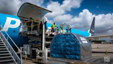 A light blue Amazon plane with side cargo door open and large metal container on the ground ready to be lifted for loading.