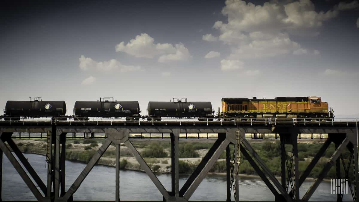 A photograph of a train hauling tank cars over a bridge.