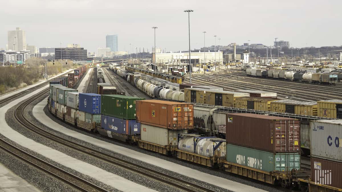 A photograph of a rail yard with parked railcars and intermodal containers.