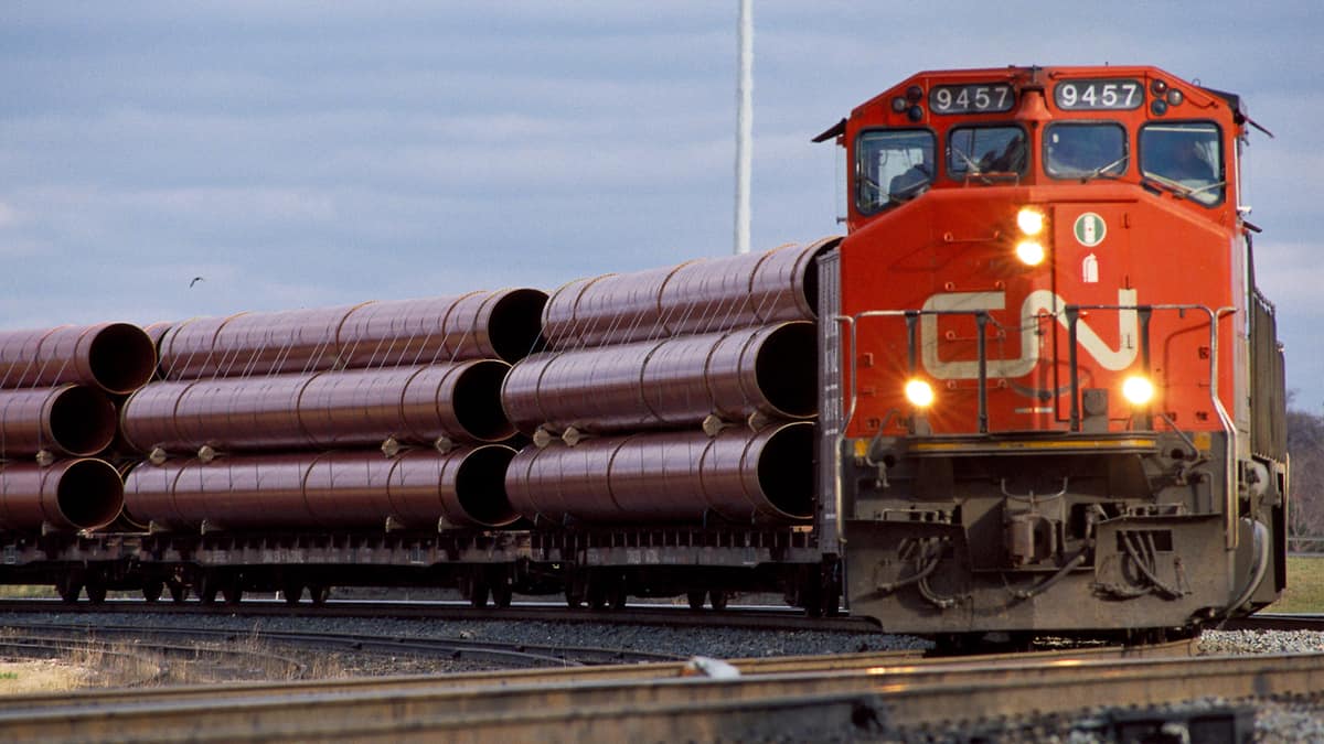 A photograph of a CN train hauling large metal pipes.