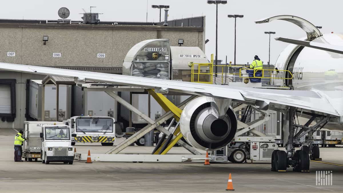 Wing of a plane viewed from behind the plane, with cargo being loaded in side door.