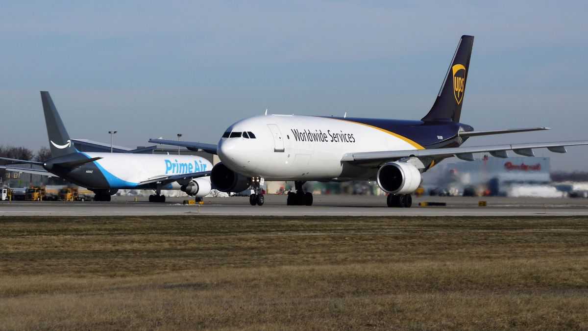 White jets with brown and blue tails at airport passing in opposite directions. Amazon and UPS planes.