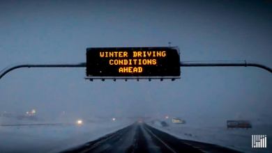 "Winter Driving Conditions Ahead" sign above a snow-covered highway.