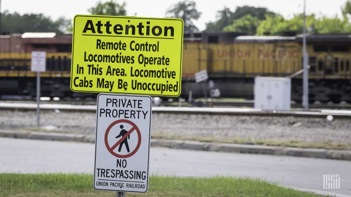 A photograph of a train in a yard. In front of it is a sign that says, Attention. Remote control locomotives operate in this area. Locomotive cabs may be unoccupied.