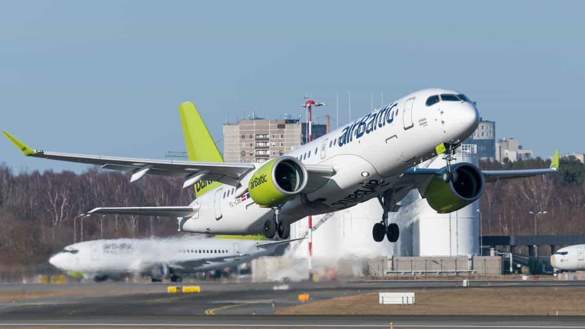 An airBaltic plane with yellow tail takes off on a clear day.