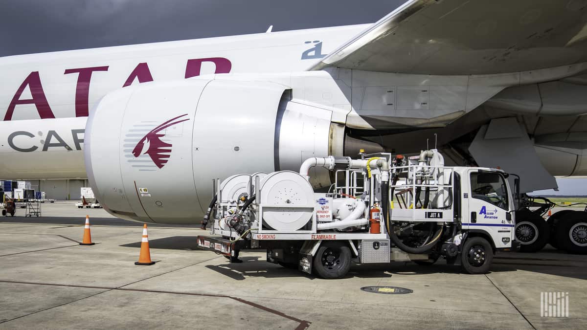 A gray Qatar Airways jet being refueled by a truck.