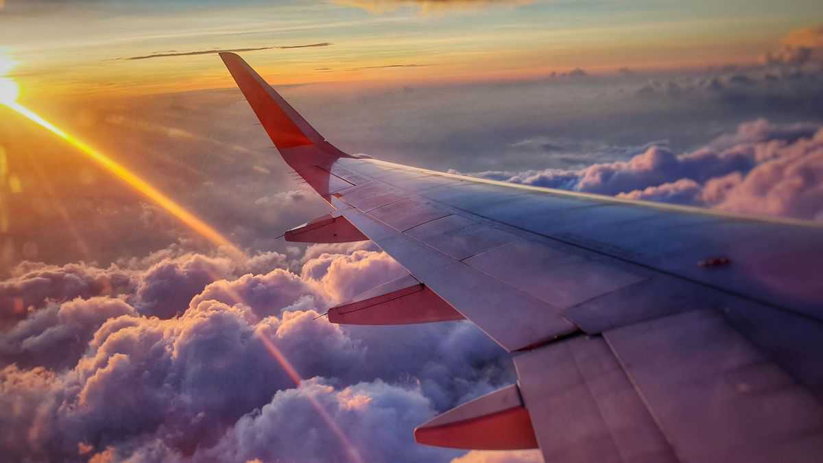 Wing view from plane in flight with sun shining in and flying over clouds.