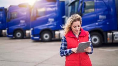 Truck driver holding tablet and checking route for new destination. In background parked truck vehicles. Transportation service.