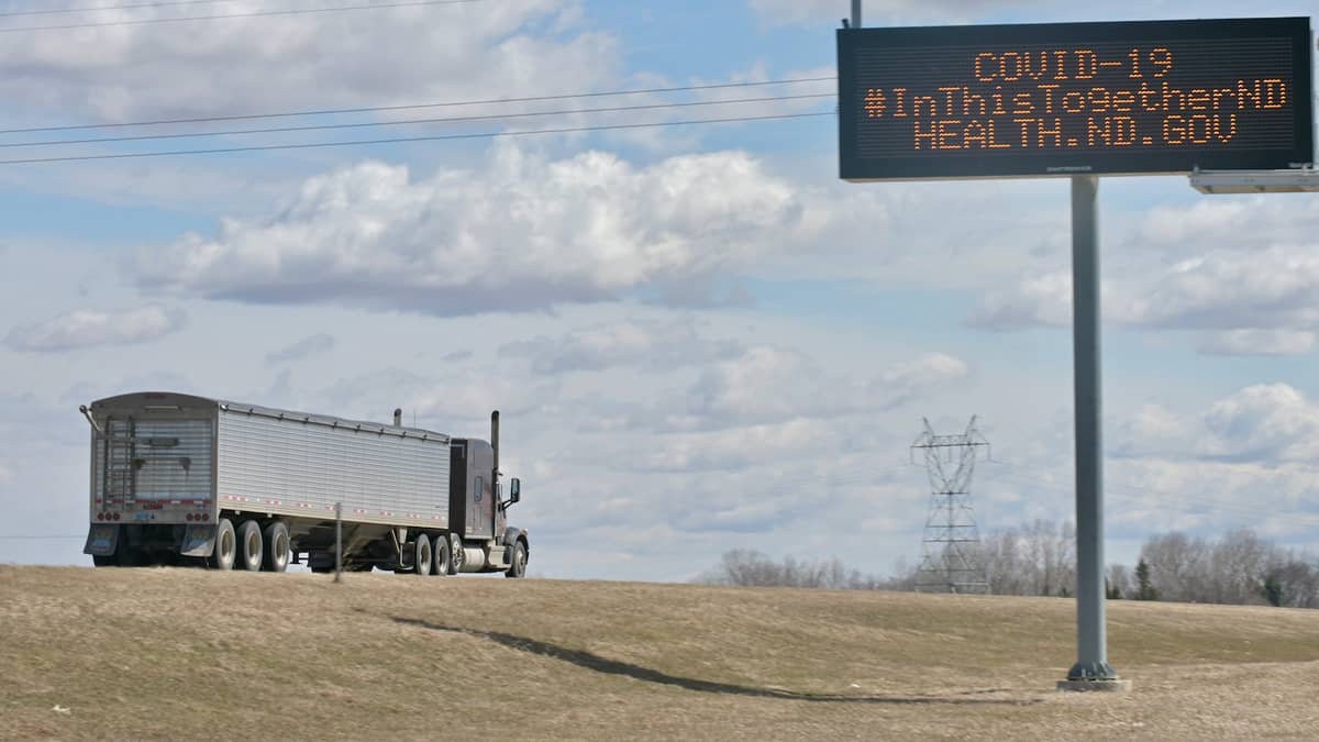 A truck passes a sign reading: COVID-19: In this together. To illustrate a story about North Dakota vaccinating Canadian truck drivers.