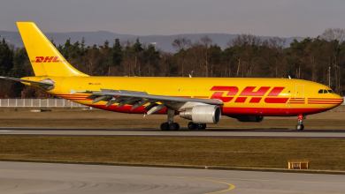 A mustard-colored DHL cargo jet on airport taxiway.