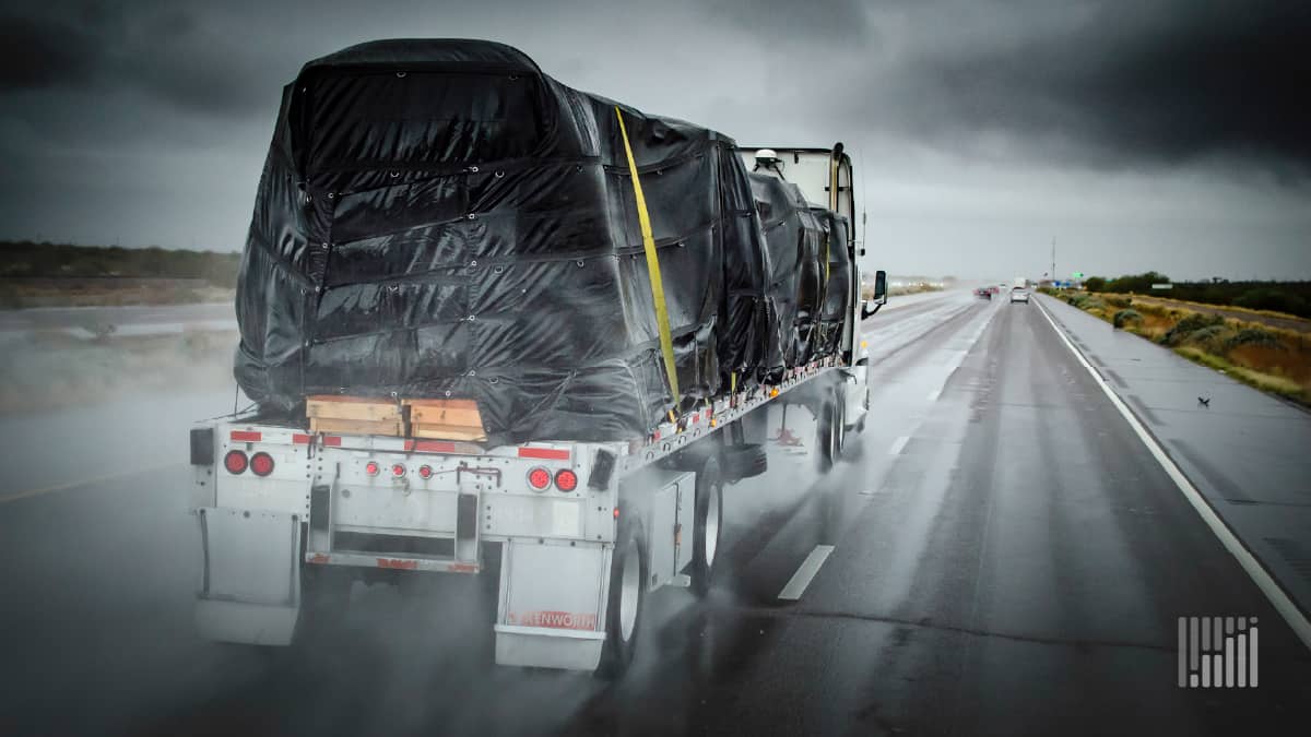 Flatbed tractor-trailer heading down road on a rainy day.