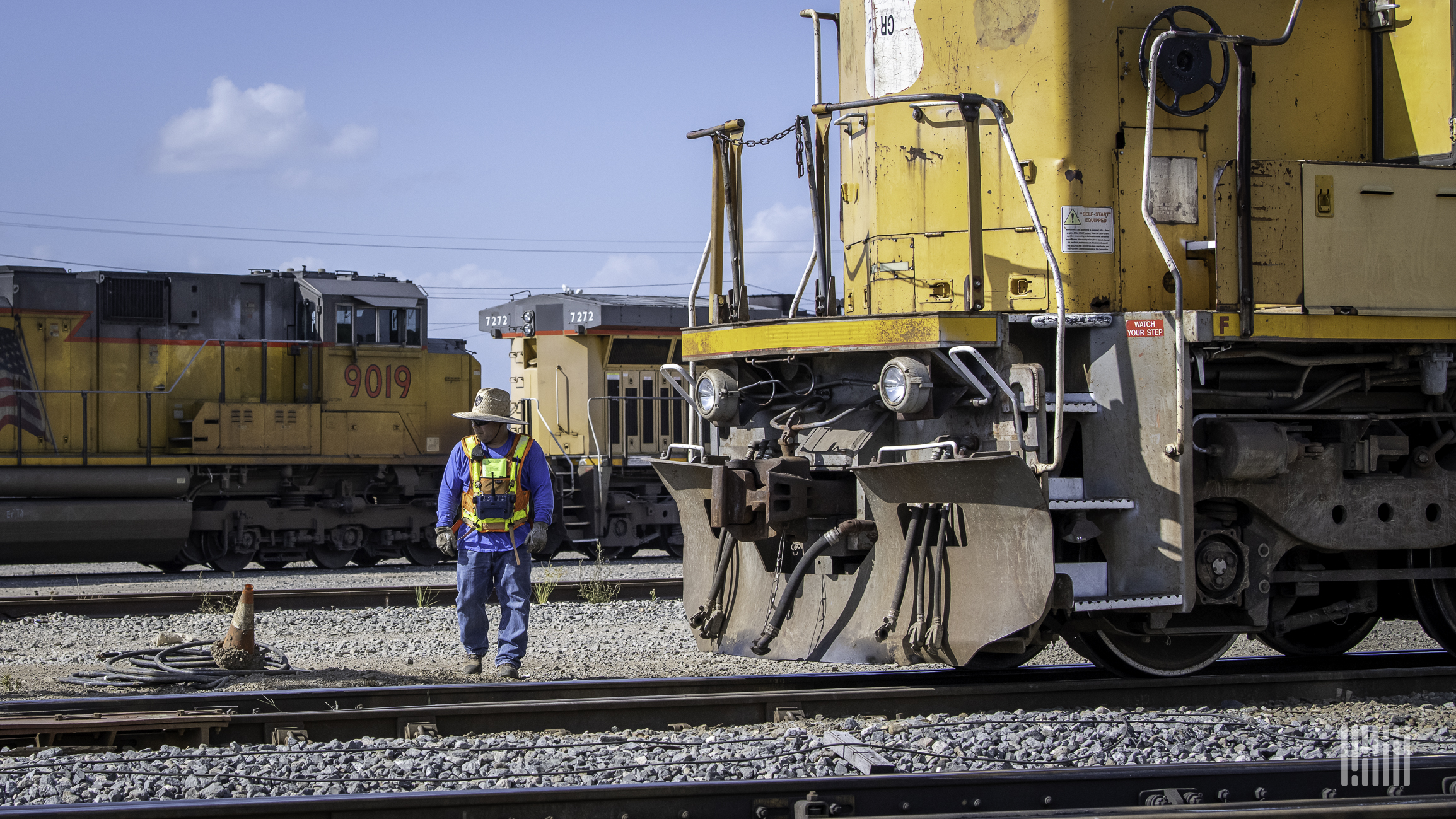A photograph of a man walking by a locomotive in a rail yard.