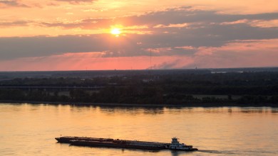 A photograph taken at sunset of a barge sailing down a river.