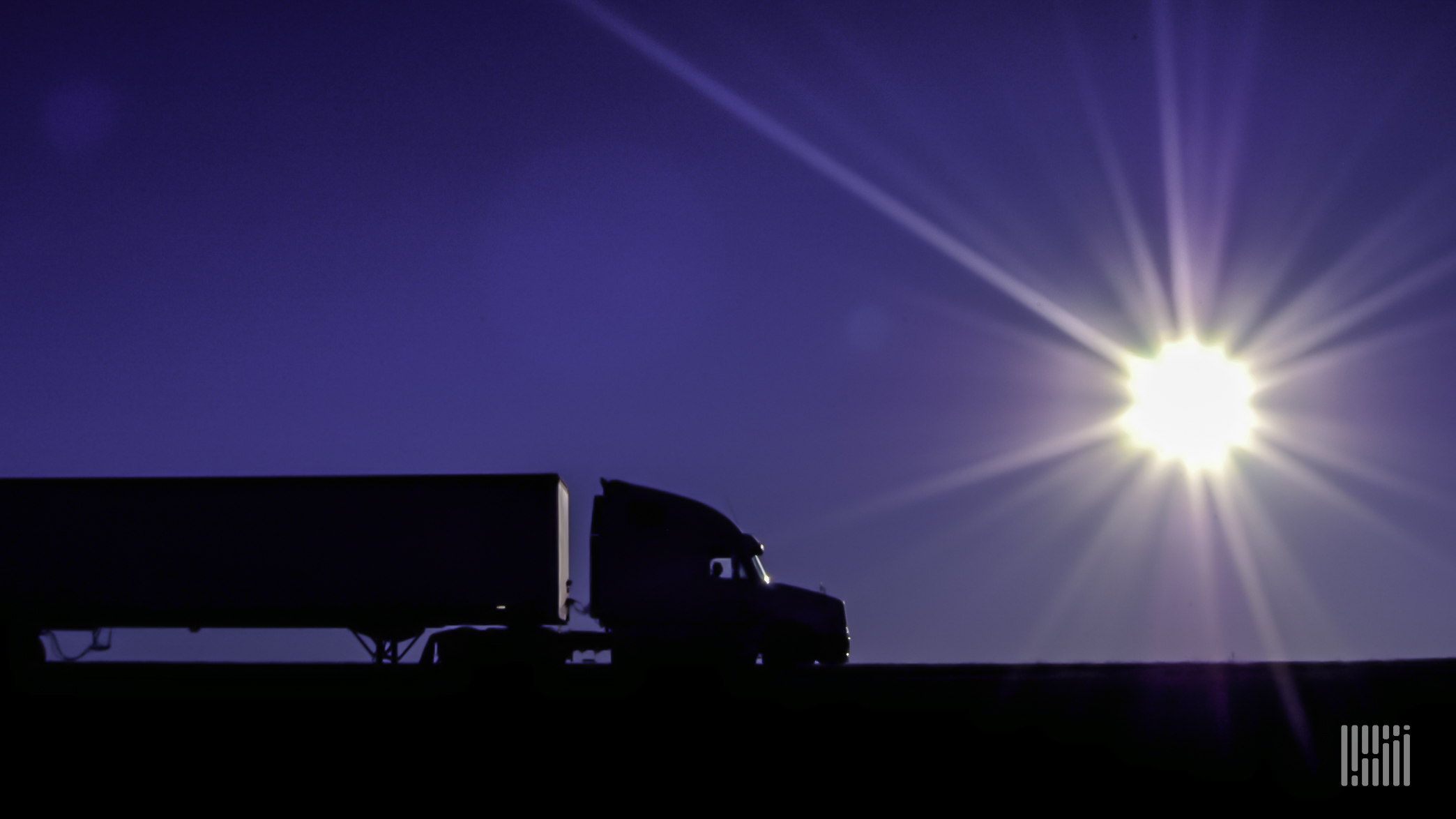 Tractor-trailer with hot sun on the horizon.