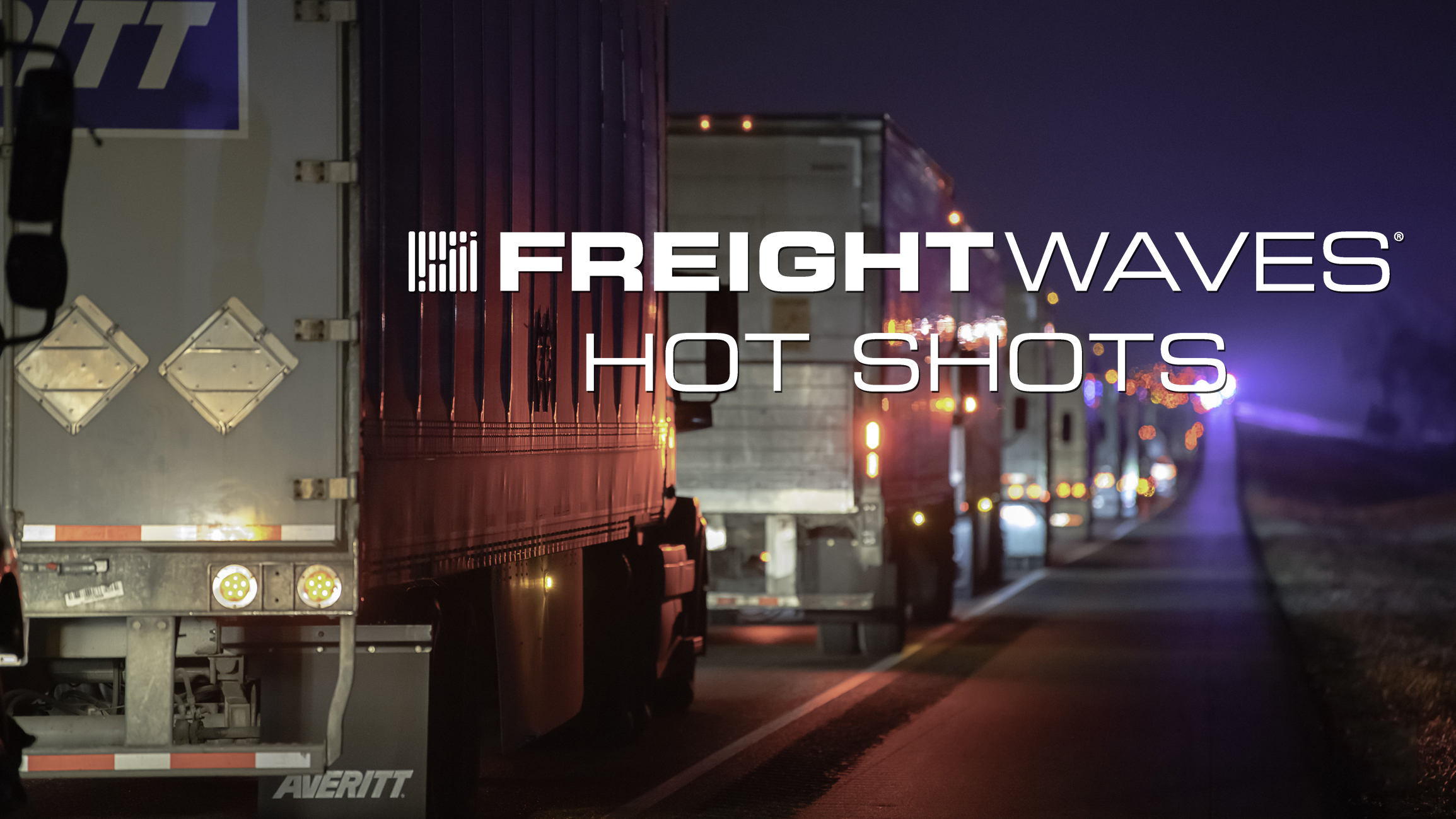 Line of tractor-trailers on a highway at night with "FreightWaves Hot Shots" logo.