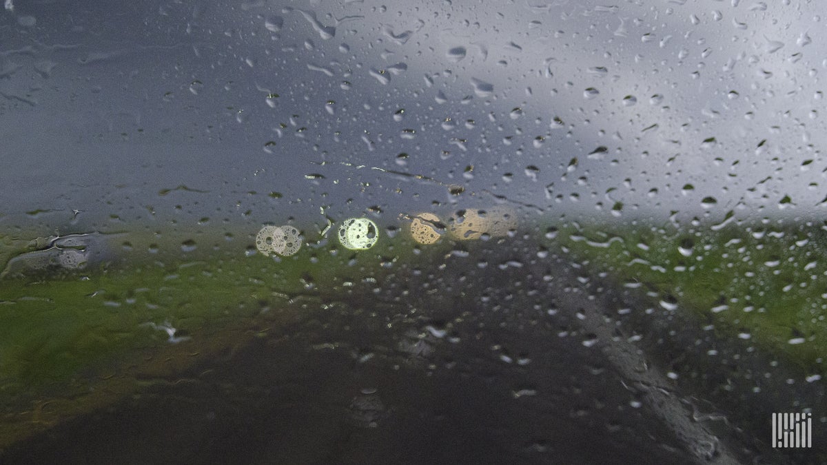 Heavy rain on windshield, looking out toward a highway.